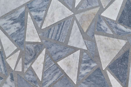 The floor or wall surface is made of triangular granite tiles. Tiles of different sizes and colors. The tiles are grey and white. The grey tiles have streaks and veins. Texture, background, backdrop.の写真素材
