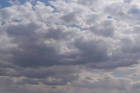 Many Cumulus and rain clouds of various shapes, sizes, and colors covered the blue sky. On the right side, the sun's rays break through from above. In the distance, the rain begins to fall.の写真素材