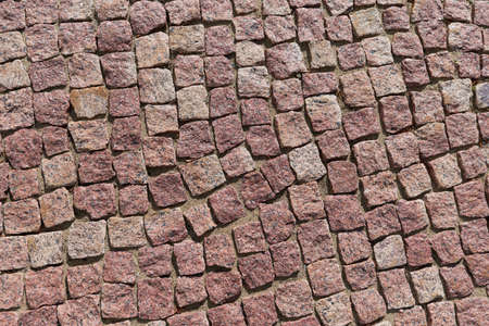 The surface of the path is paved with square-shaped granite cobblestones. The stones are laid in several rows on the sand. All tiles are uneven and of different shapes. Background, texture, backdrop.の写真素材