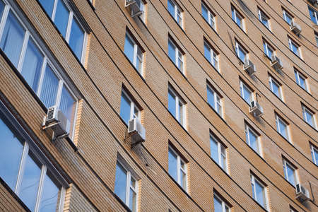 The curved wall of a brick house with many Windows and several air conditioners. Part of the building's facade is made of rounded beige bricks. The view goes up. Background, backdrop.の写真素材