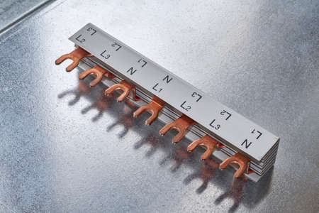 The busbar made of copper with a cutout in the form of a plug for modular electric switches lies on a metal sheet. The busbar is insulated in a special dielectric plastic or material.の写真素材