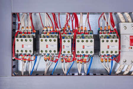 Several contactors and an automatic switch are arranged in a row in the electrical Cabinet. Wires are connected to the contactors. Front additional contacts are located on the front of the starters.の写真素材