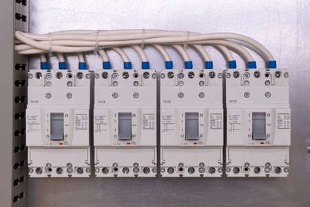 Four large power circuit breakers are mounted on a panel in a row in the electrical Cabinet. Cables are connected to the switches. The wires are carefully laid in a perforated cable channel.の写真素材