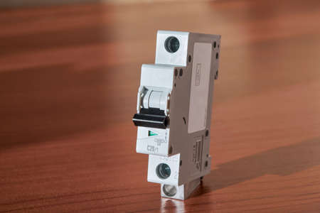 Electric single-pole modular circuit breaker on the table surface in red color. The switch has a green pin status indicator. The switch lever is black. Protection of electrical wiring in the building.の写真素材