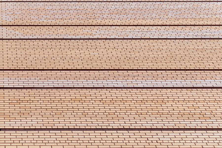 A brick wall with dark horizontal seams of a large, high building. View of the building wall with perspective. Background, texture, and backdrop.の写真素材