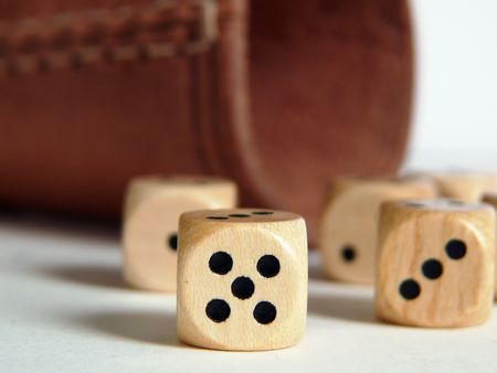 Wooden dices on the white table with brown leathery dice box in the background