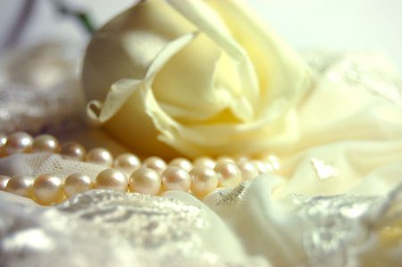 Delicate white rose and a pearl necklace on a lacy bridal lingerieの写真素材
