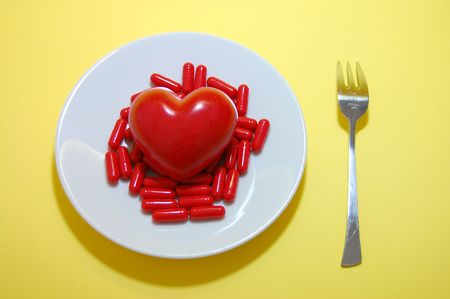 Red pills, a red heart on a white plate and a fork on a yellow backgroundの写真素材