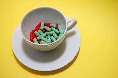 A cup of red and green pills on a yellow backgroundの写真素材
