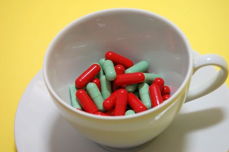 A cup of red and green pills on a yellow backgroundの写真素材