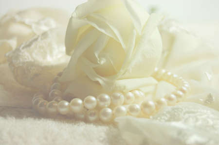 Delicate white rose and a pearl necklace on a lacy bridal lingerieの写真素材