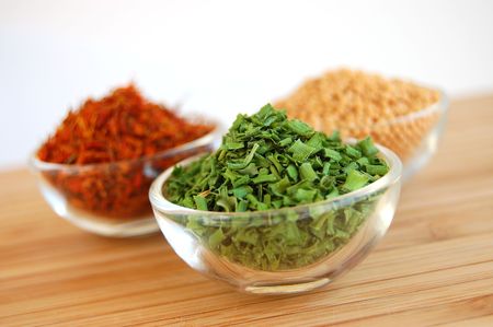 Three glass containers with saffron, mustard seed and chive on a wooden cutting deskの写真素材