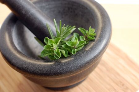 Freshly picked oregano and rosemary in a gray mortar on a wooden kitchen desk