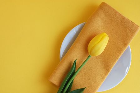 Yellow tulip and a napkin on a white plate