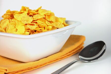 Cornflakes in a white bowl on a yellow napkin and a spoon