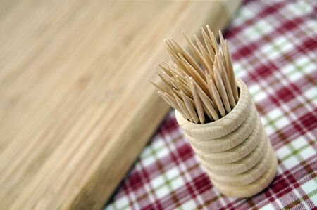 Wooden toothpicks in a wooden holder on a red and white checked tableclothの写真素材