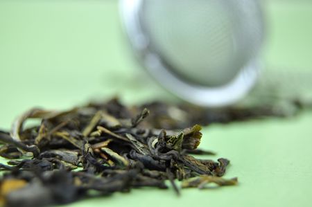 Aromatic tea leaves and a tea strainer on a green backgroundの写真素材