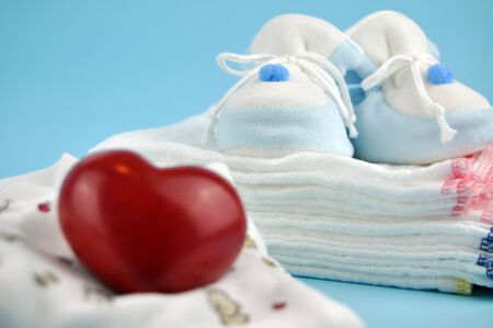 Red wooden heart with baby shoes on a pile of white cotton diapers in the backgroundの写真素材