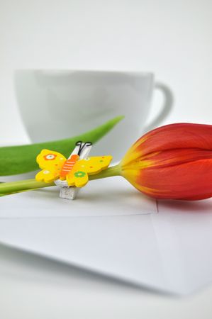 Red tulip and wooden butterfly on a white envelope with a cup of tea in the backgroundの写真素材