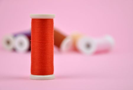 Orange thread with a pile of colorful spools in the backgroundの写真素材