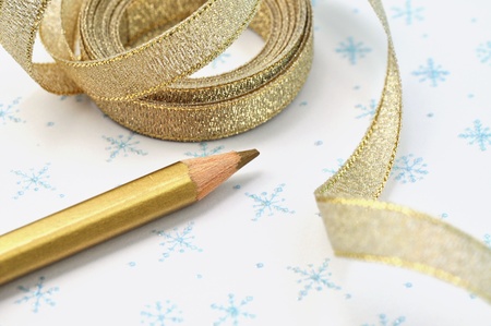 Golden pencil and ribbon on Christmas paperの写真素材