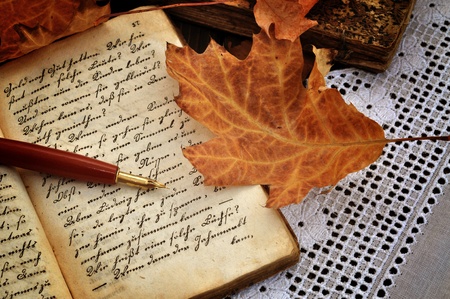 Fountain pen on old handwritten book with autumn leaves on a lacy tableclothの写真素材