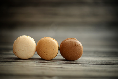 Three brown macaroons in a line on a wooden tableの写真素材