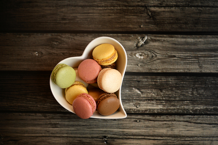 Colorful macaroons in a heart shaped white bowl on dark wood backgroundの写真素材