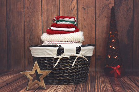 A pile of folded red, white and green knit Christmas clothes in a wicker basket with Christmas treeの写真素材