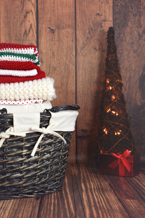 A pile of folded red, white and green knit Christmas clothes in a wicker basket with Christmas treeの写真素材