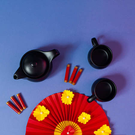 Chinese New Year composition with teapot, teacups, red paper fan and firecrackers on pastel blue background.の写真素材