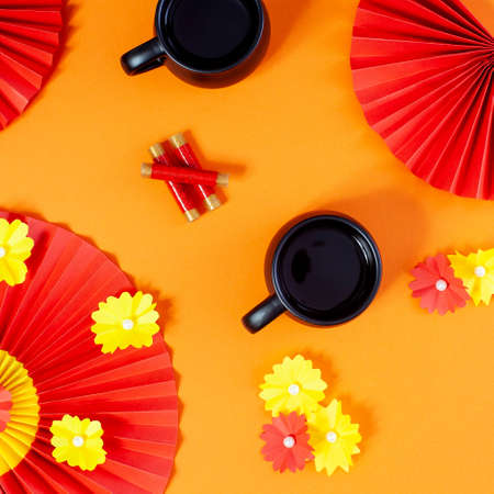 Chinese New Year composition with teacups, red paper fans with flowers and firecrackers on pastel orange background.の写真素材