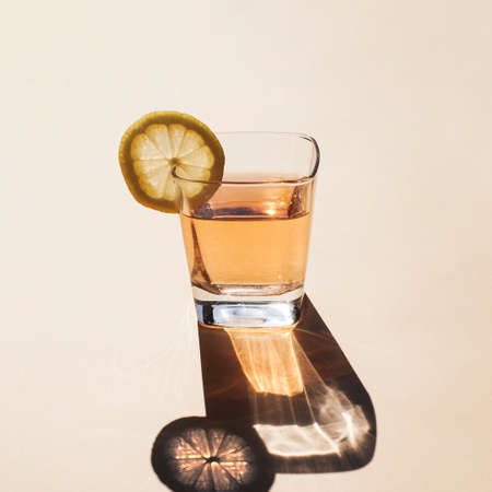 Glass of beverage with lemon slice on hot summerâs day. Simple square composition with long shadows and light reflections.の写真素材