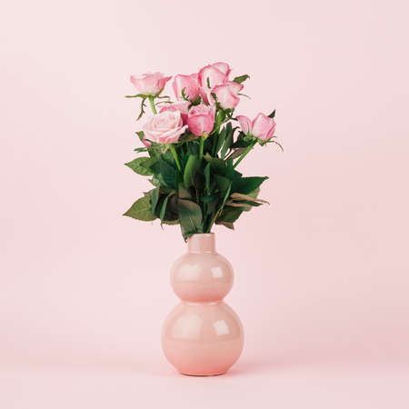 Bouquet of pink roses in peach vase on continuous pastel pink background. Simple central composition with soft light.の写真素材