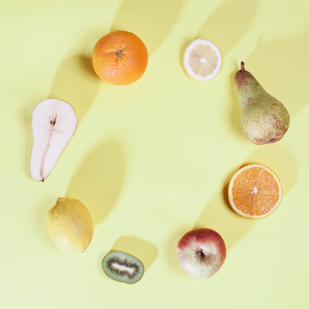 Fruit circle. Row of different fruit and slices. Square composition with long light shadows on gentle pastel yellow bacground.の写真素材