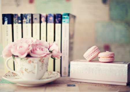 Roses in a vintage tea cup with macaroons and booksの写真素材