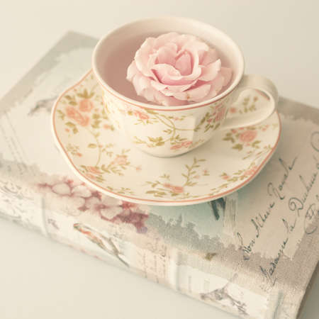 Rose in a vintage tea cup over antique bookの写真素材