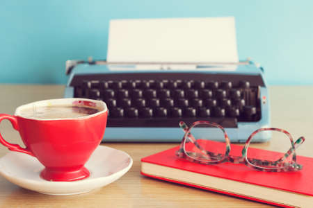 Vintage typewriter, notebook and eyeglasses over coffee cup