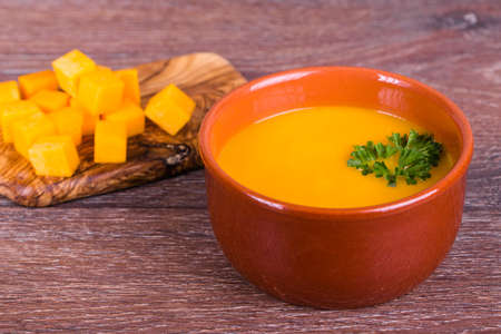 Bowl of pumpkin soup with parsley on wooden background