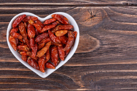 Chili pepper in a bowl in the form of heart on a wooden backgroundの写真素材