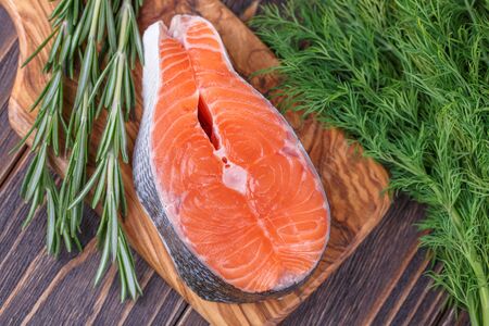 Fresh raw salmon fish steaks with fresh herbs on wooden background