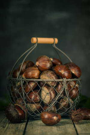 Raw chestnuts on a wooden background in an iron basket. Rustic styleの写真素材