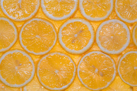 Slices of fresh, yellow lemon under water as a textured background.