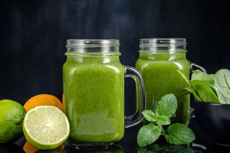 Healthy green smoothie with spinach, mango, orange, lime, apple, citrone in glass jars.