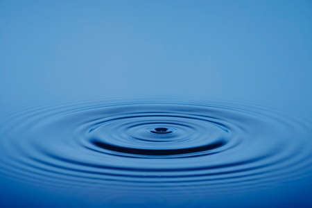 Closeup Water drop or splash falling on the surface of the water and beautiful circular wave ripple, water concept, with blue backgroundの写真素材