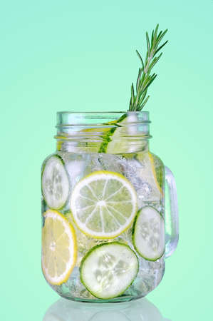 Jar mug with fresh organic detox cucumber water with lime and lemon on green background.