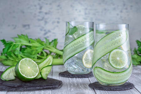 Glass with fresh organic detox cucumber water with lime and lemon on gray background.
