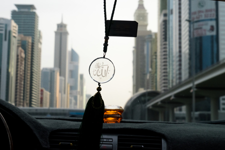 Allah symbol hanging in a car with the city of Dubai on the backgroundの写真素材
