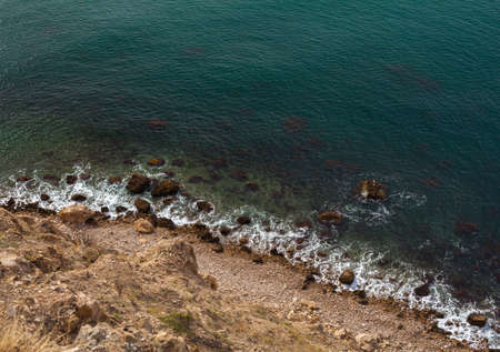 sea wave washes yellow beach of pebbles sea occupies a large area of the picture is in the corner of coastの写真素材