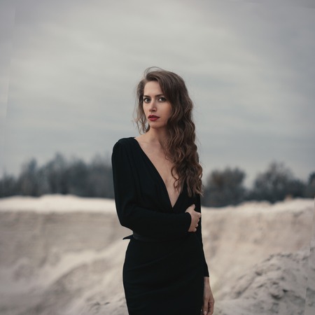 Beautiful girl in in black vintage dress with curly hair posing on the sand. Woman in retro dres....